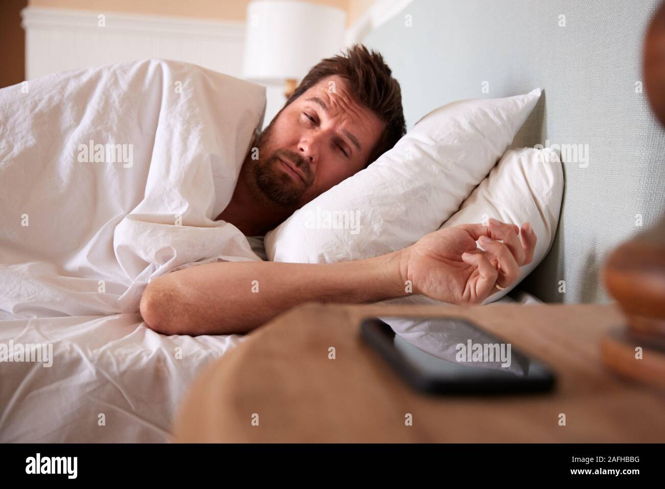 Mid adult man asleep in bed, looking at the smartphone on the bedside table in the foreground Stock Photo