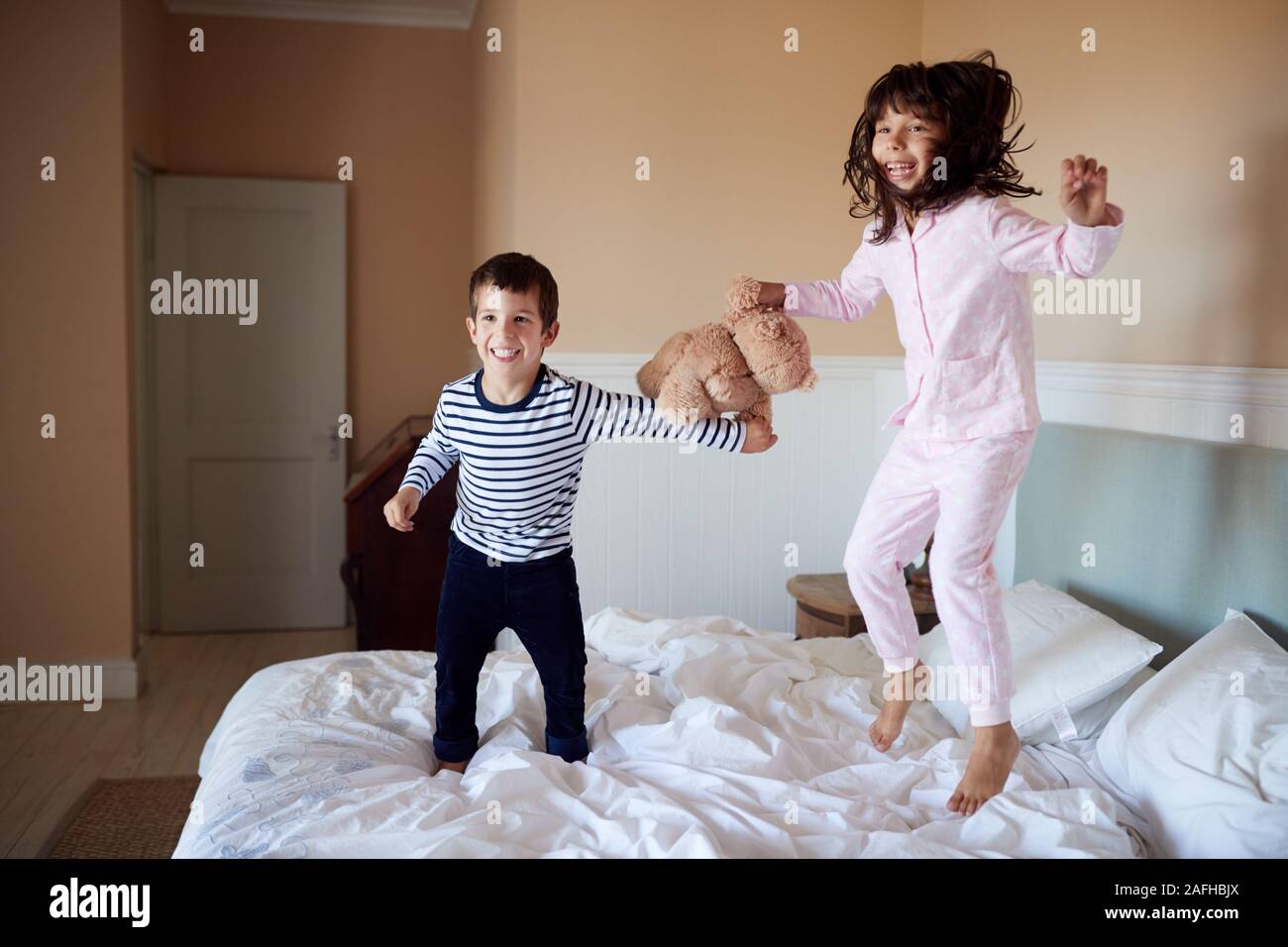 Brother and sister having fun bouncing on their parents’ bed in their pyjamas, full length Stock Photo