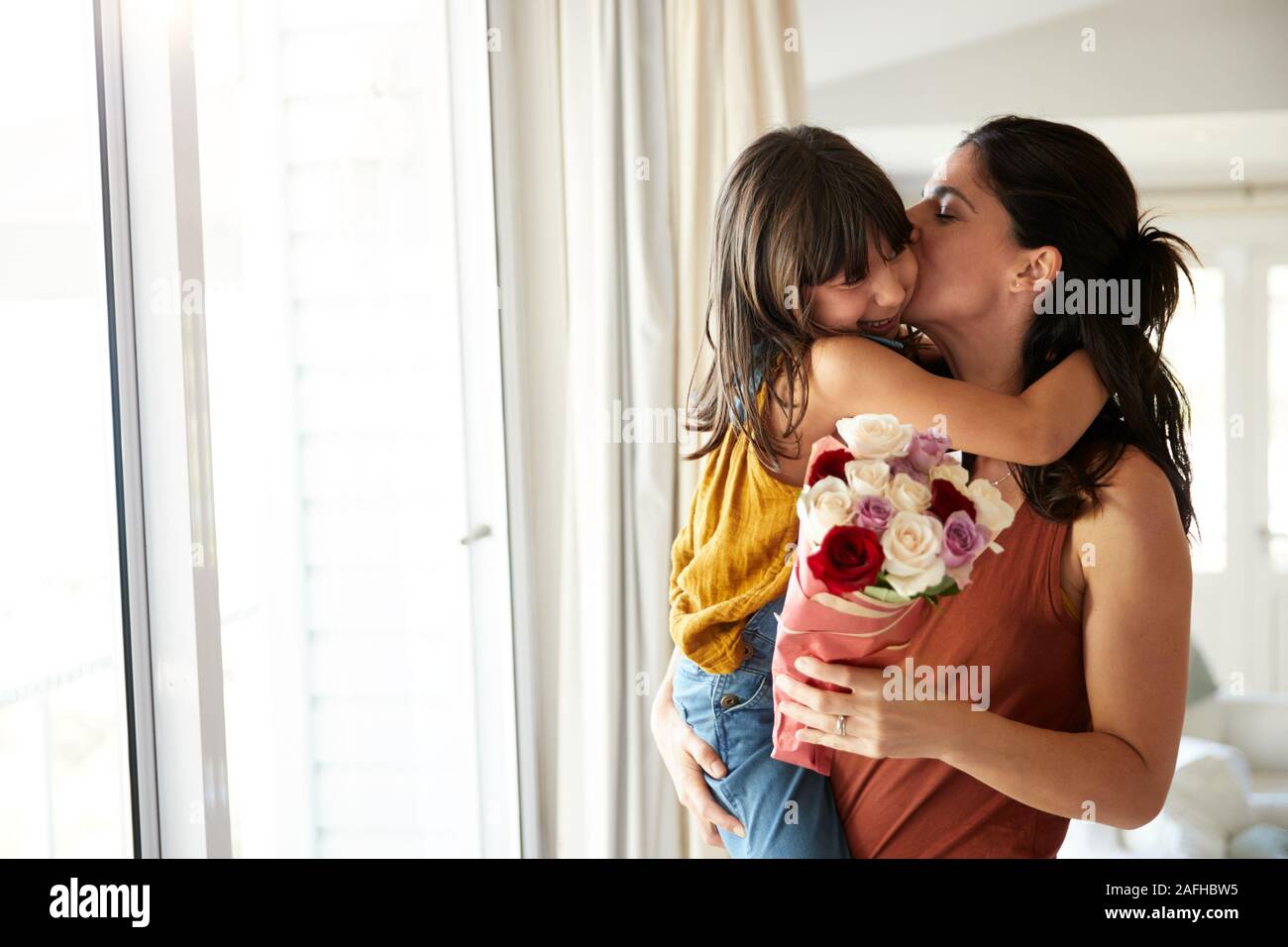 Mid adult woman holding her daughter, who’s given her a bunch of flowers on her birthday, waist up Stock Photo