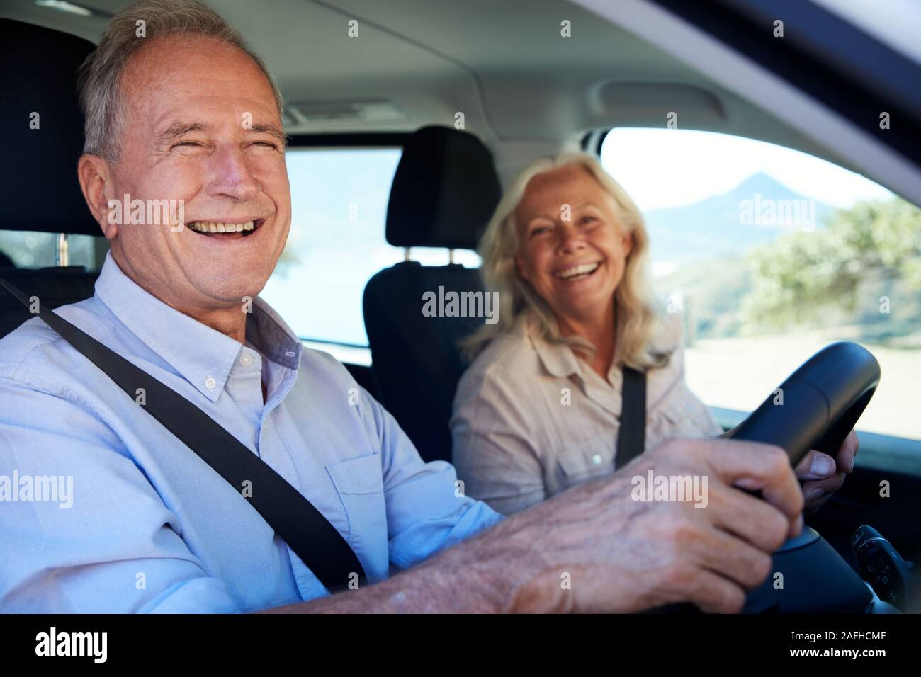 Happy senior white couple driving in their car, smiling to camera, side view, close up Stock Photo