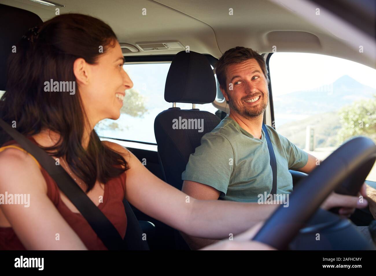 Mid adult white woman driving car, smiling to her husband in the front passenger seat, side view Stock Photo