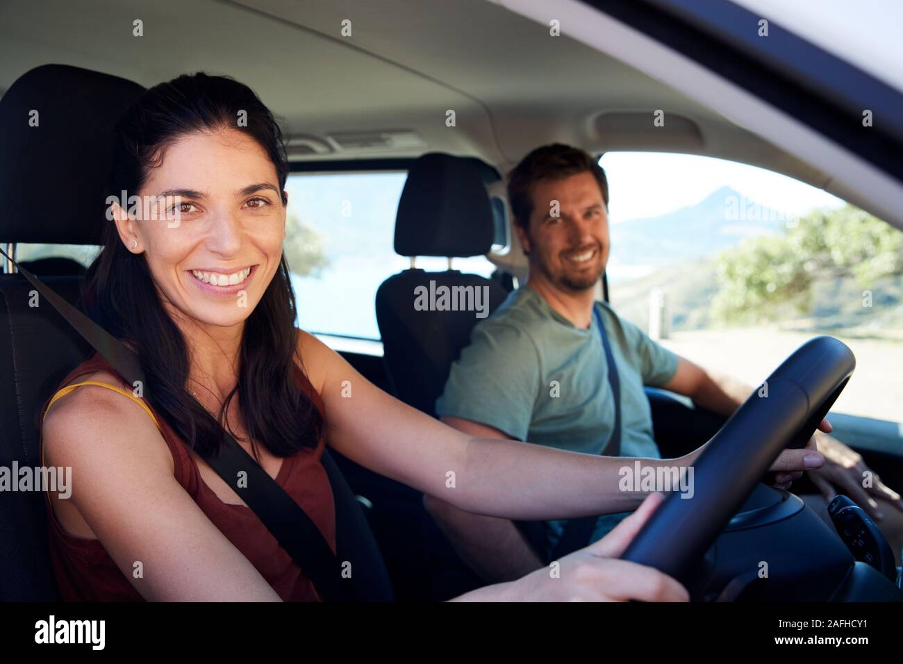 Mid adult white woman driving car, her husband in front passenger seat, smiling to camera, side view Stock Photo