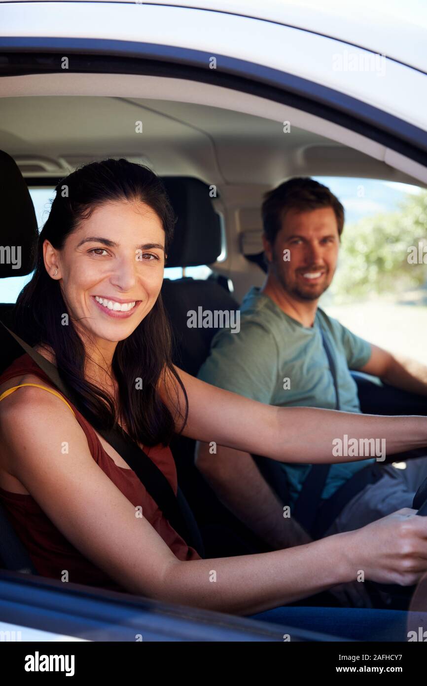 Mid adult white woman driving car, husband in front passenger seat smiling to camera, vertical Stock Photo