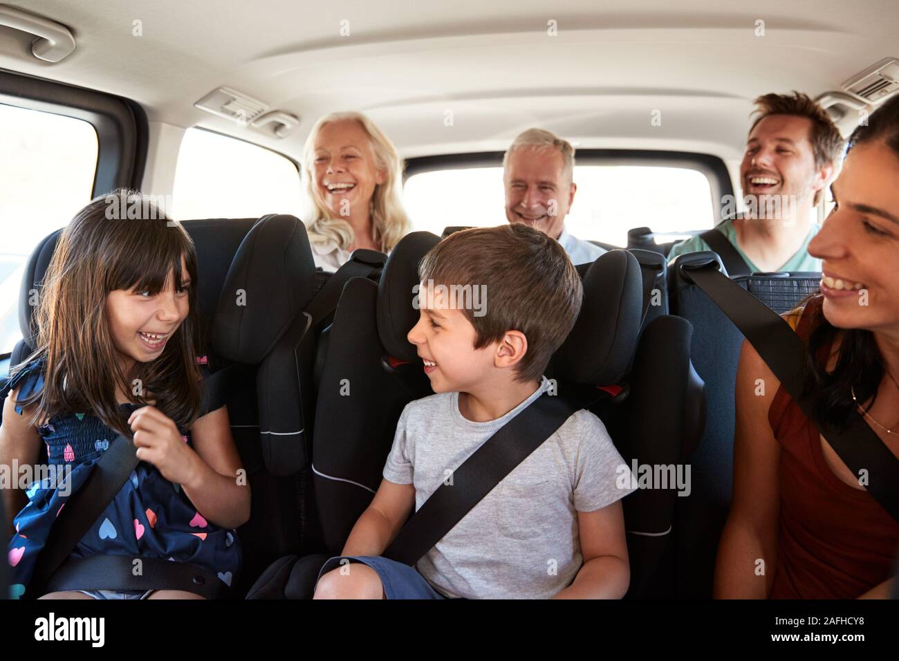 Three generation white family sitting in two rows of passenger seats in a car, looking at each other Stock Photo