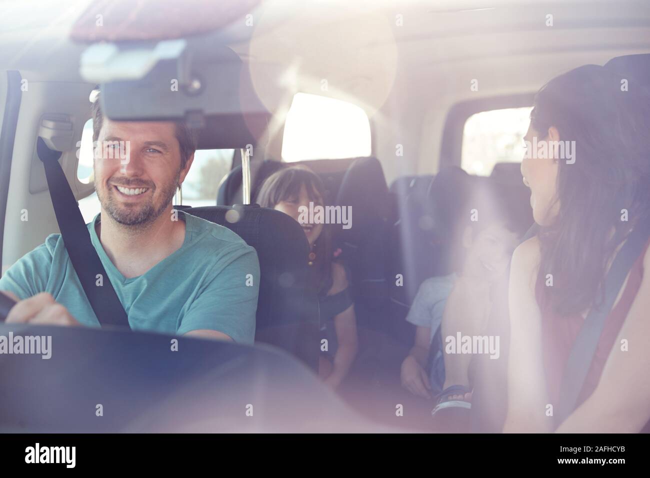 Young white family of four in their car, mum turning to speak to kids, seen through front windscreen Stock Photo