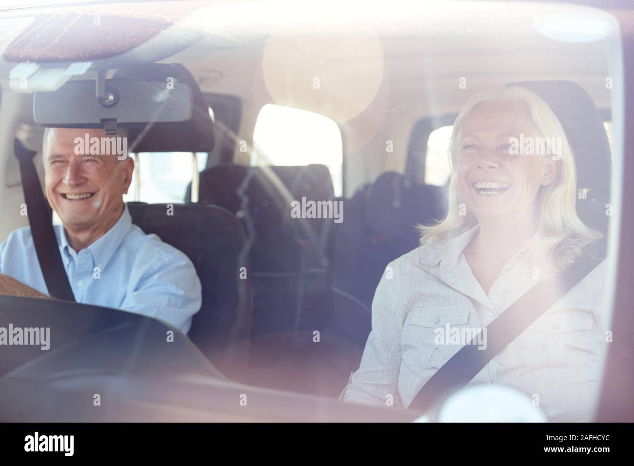 Senior white couple driving in their car on a sunny day, seen through front windscreen Stock Photo