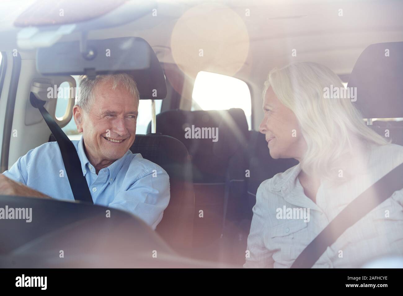 Senior white couple driving in their car smiling to each other, seen through front windscreen Stock Photo