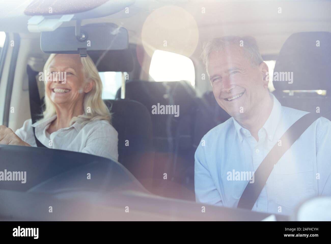 Happy senior white woman driving, her husband in front passenger seat, seen through front windscreen Stock Photo