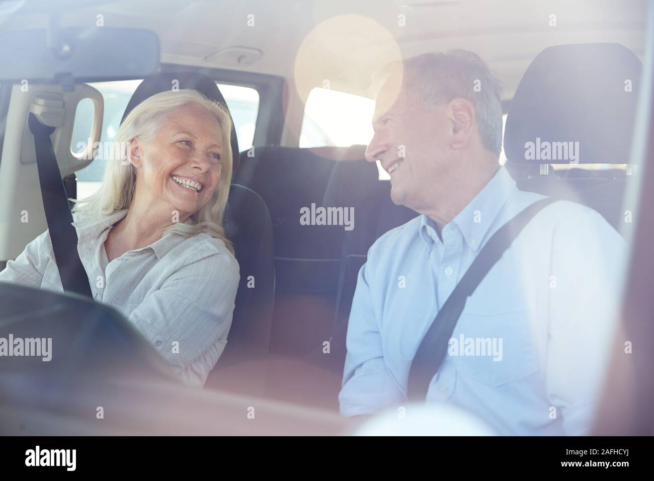 Happy senior white couple driving in their car smiling at each other, seen through front windscreen Stock Photo