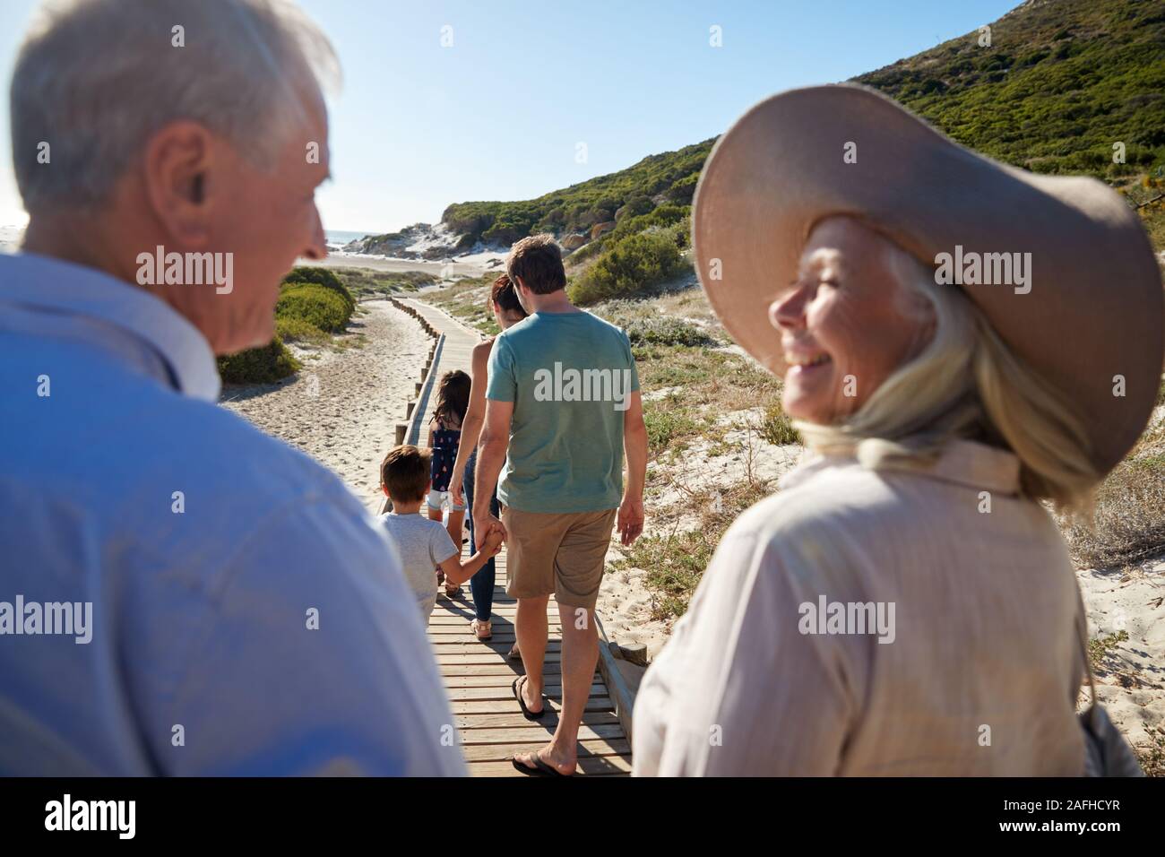 Three generation white family walking on a beach, grandparents in the foreground, over shoulder view Stock Photo