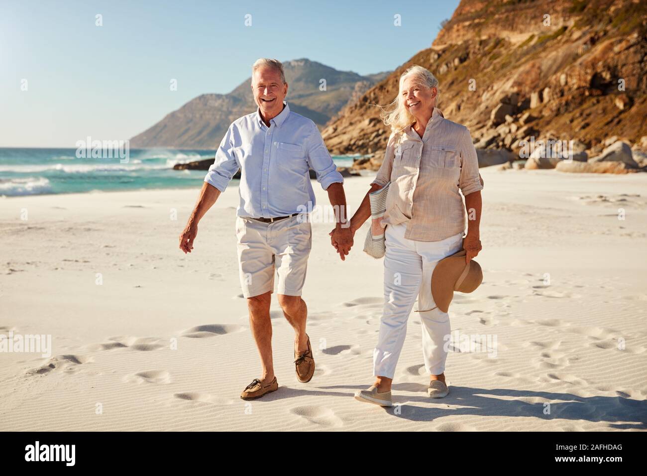 Senior white couple walking on a beach together holding hands, full length, close up Stock Photo