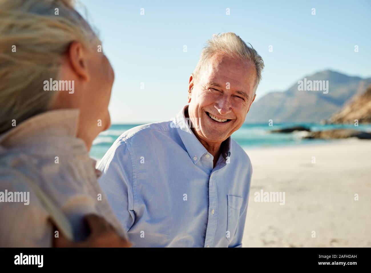 Senior white couple walking on a beach, looking at each other and smiling, waist up, close up Stock Photo