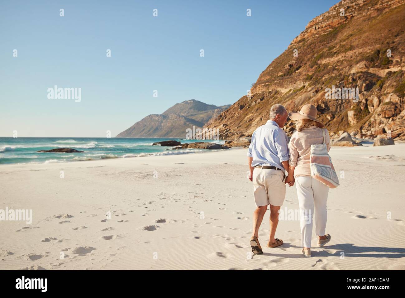 Senior white couple walking on a beach together holding hands, full length, back view Stock Photo