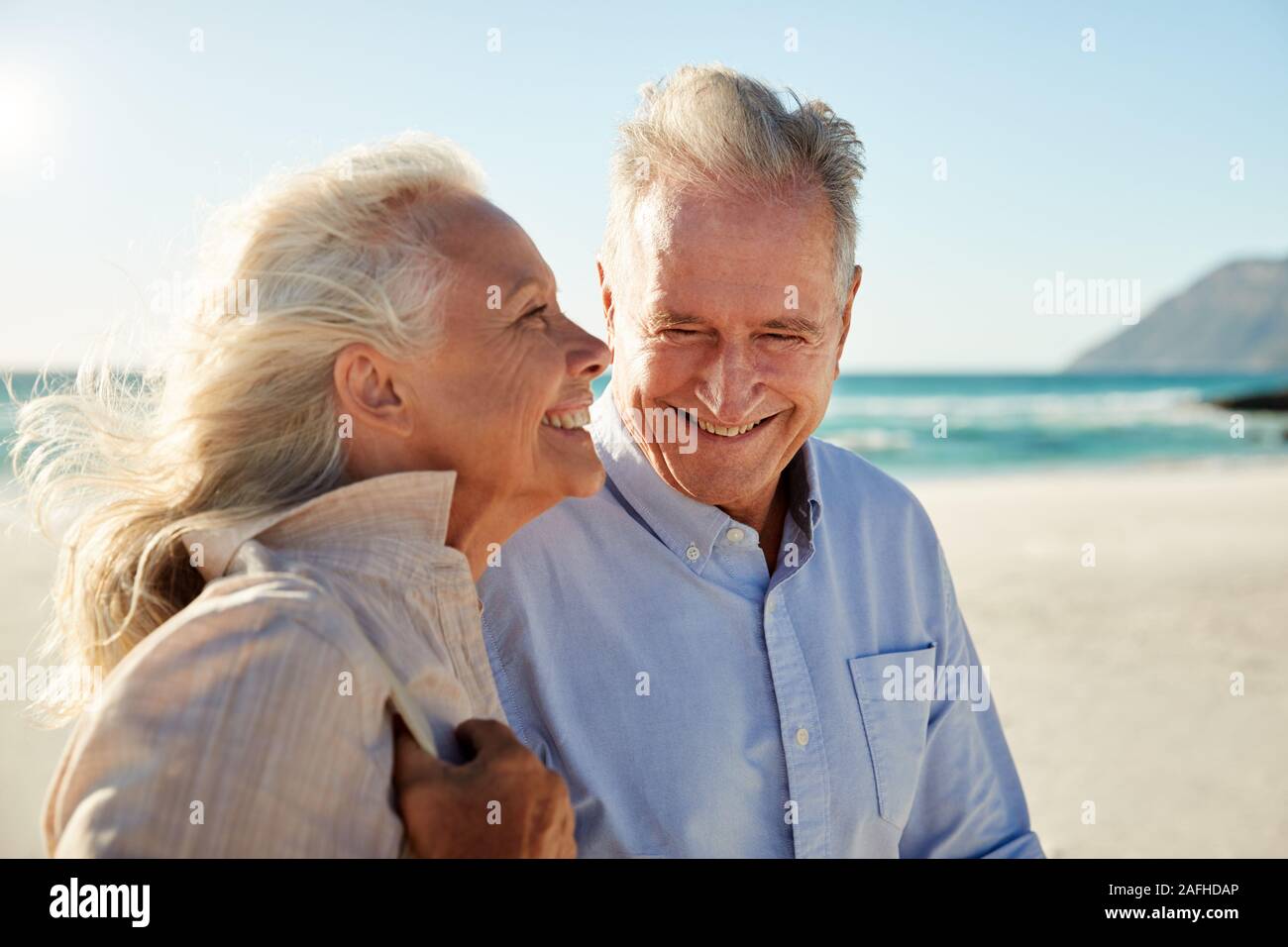 Senior white couple walking on a sunny beach, waist up, side view, close up Stock Photo