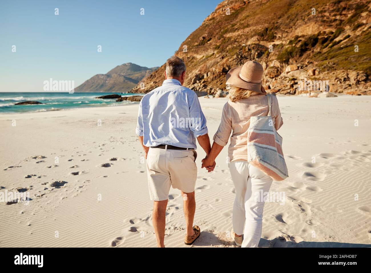 Senior white couple walking on a beach holding hands, back view, three quarter length, close up Stock Photo