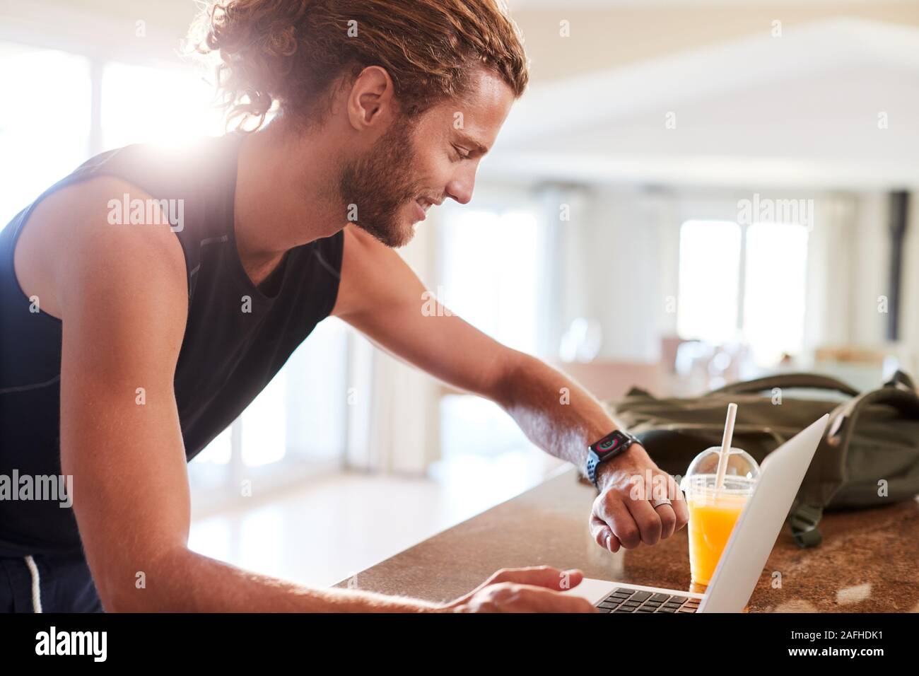 Millennial white man checking fitness app on watch and laptop after a workout, side view Stock Photo