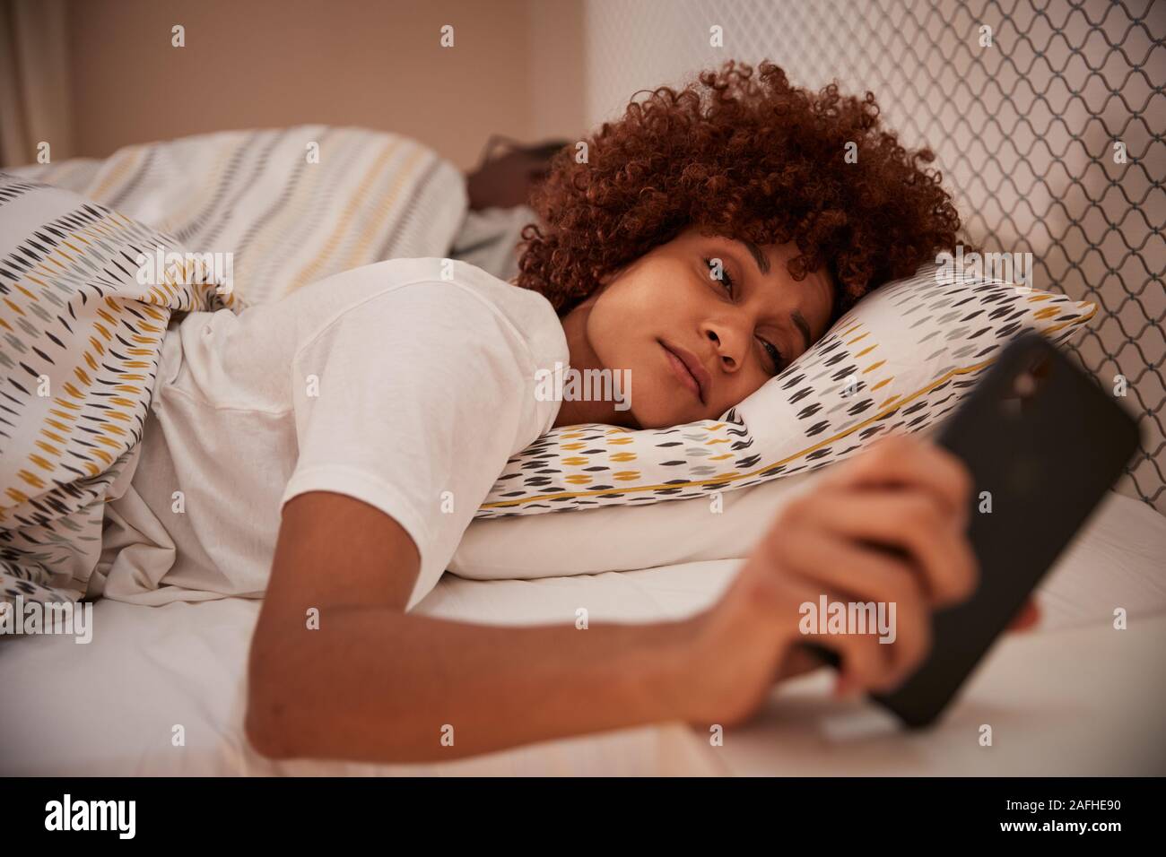 Millennial African American woman half asleep in bed, looking at her smartphone, close up Stock Photo