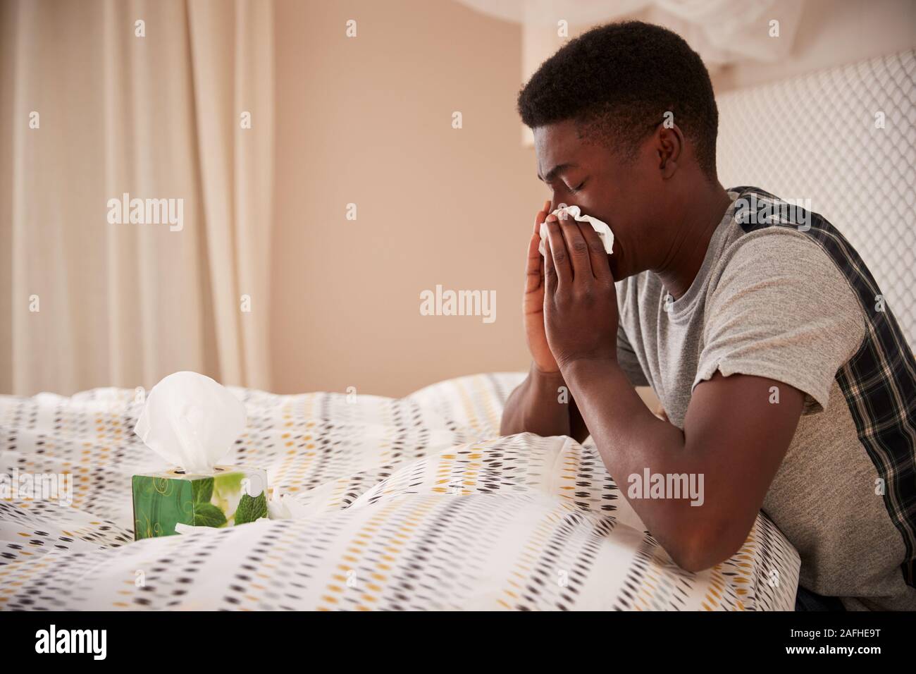 Millennial African American man sitting up in bed blowing nose, side view, close up Stock Photo