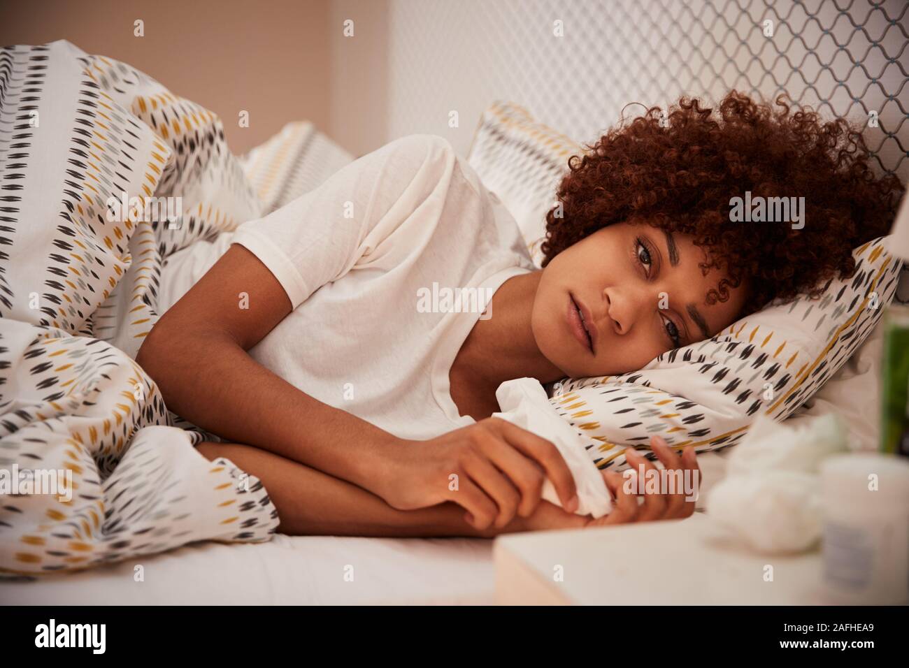 Millennial African American woman lying ill in bed looking to camera, close up Stock Photo