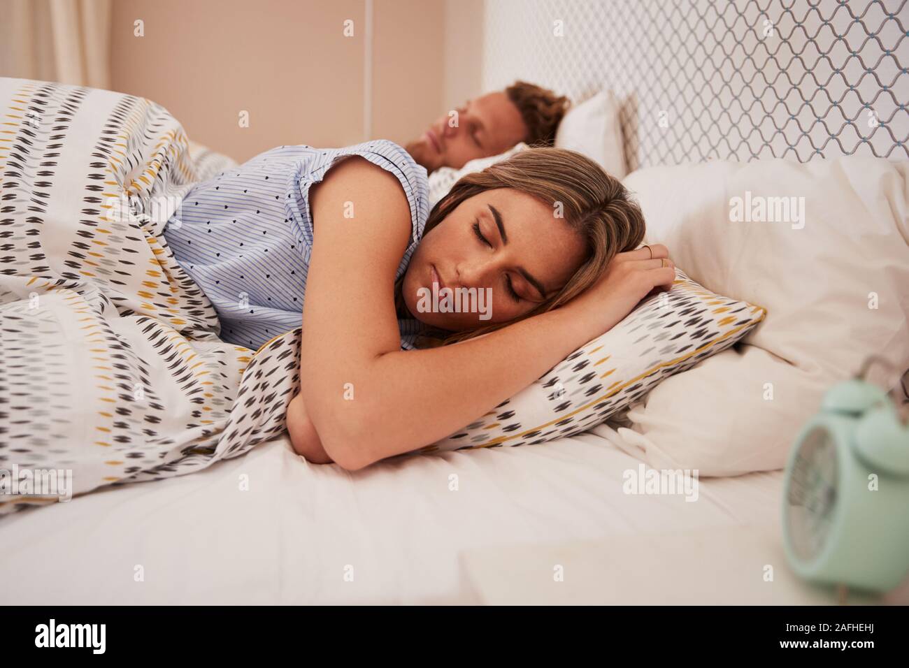 Millennial white couple asleep in bed, alarm clock in the foreground, close up Stock Photo