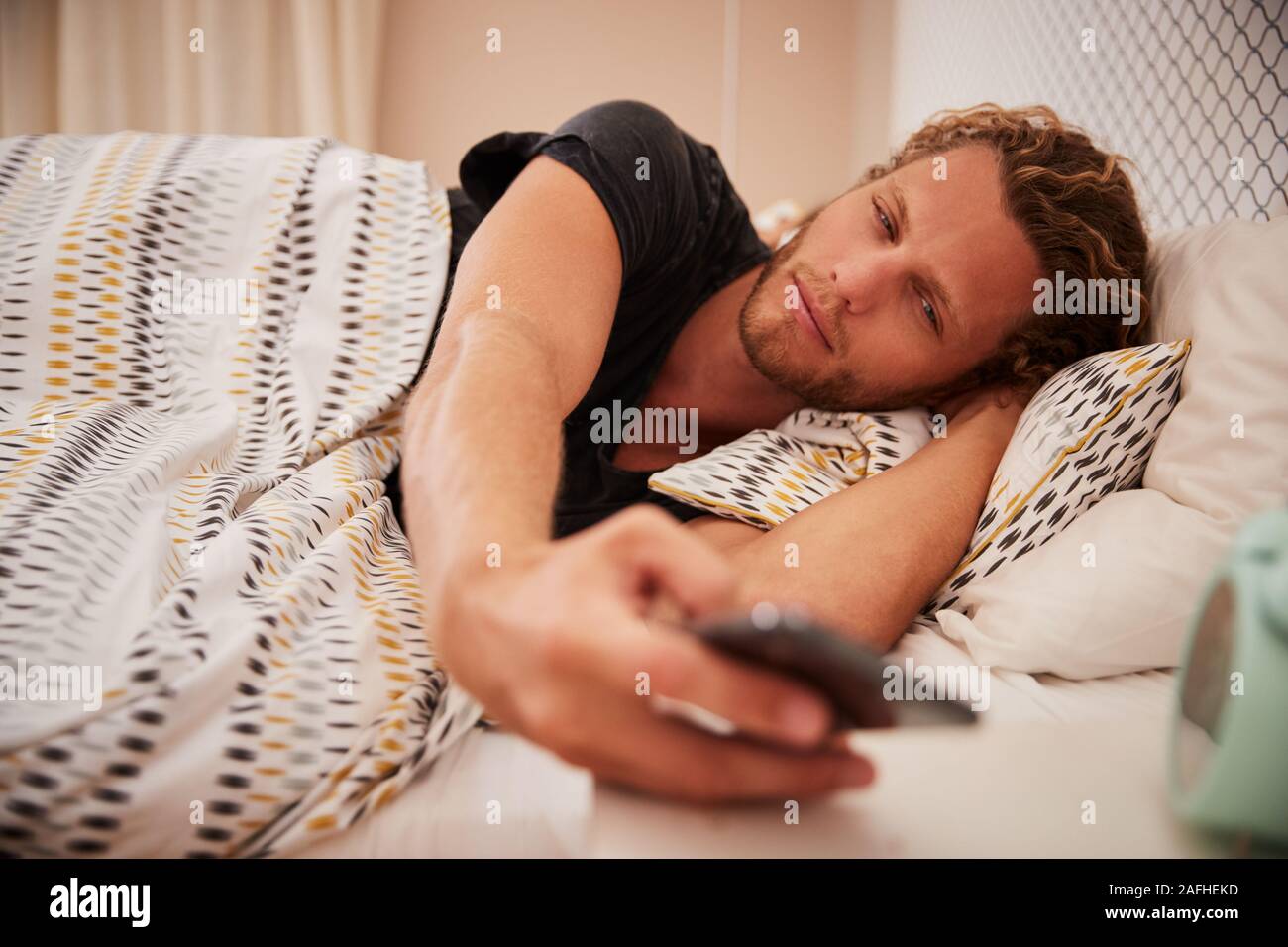 Millennial white man waking up in bad using smartphone, close up Stock Photo