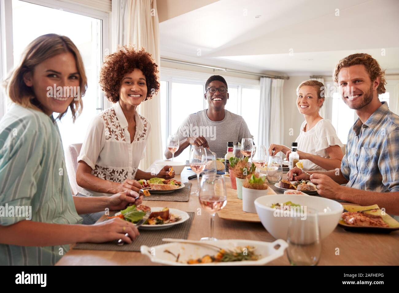 A group of millennial friends sitting at a table eating lunch, looking to camera, backlit Stock Photo