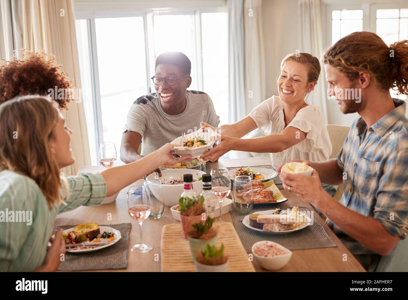 Two young adult women passing a dish across the dinner table during lunch with friends, close up Stock Photo