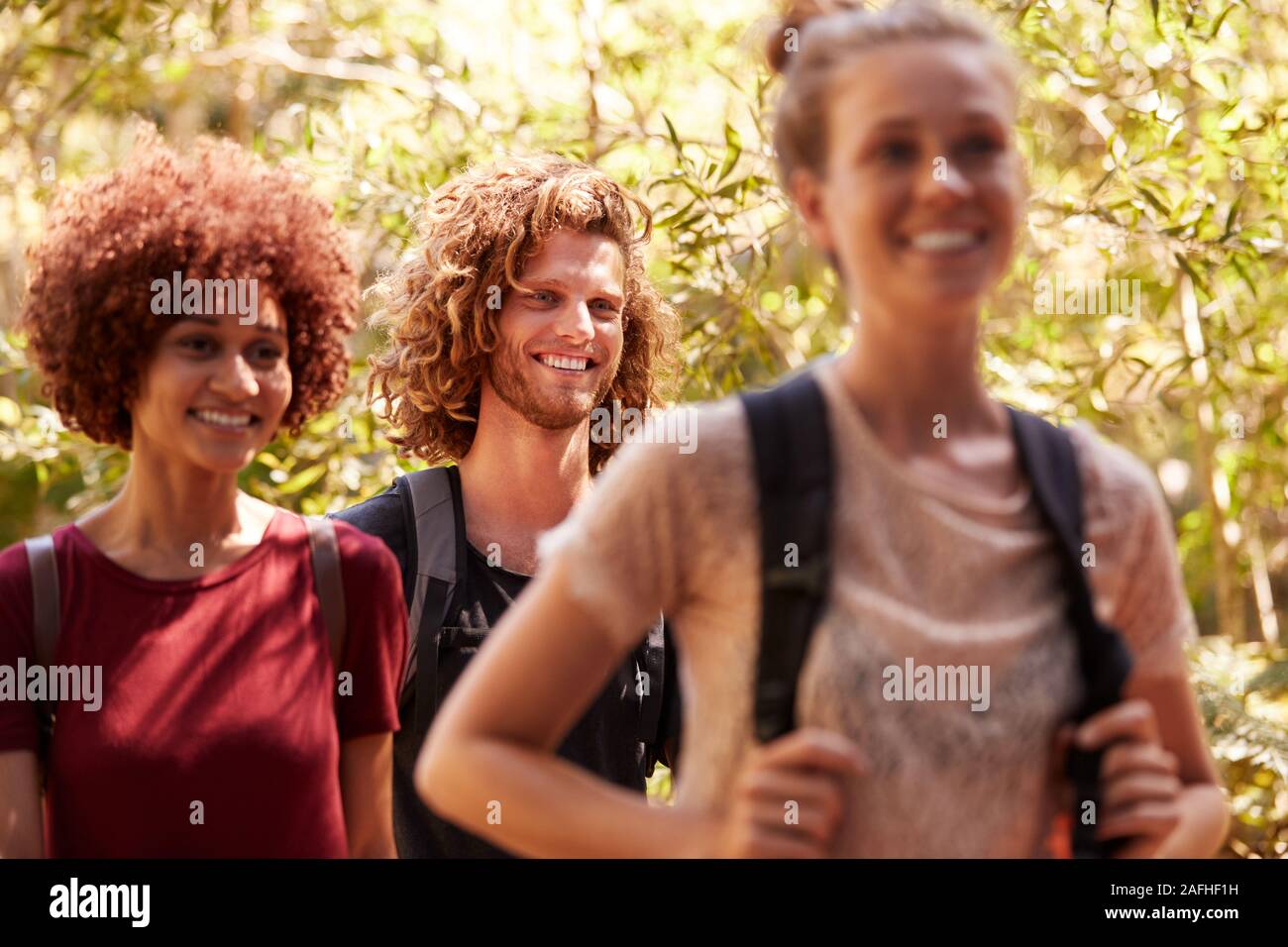 Three happy millennial friends wearing rucksacks on a hike in a forest, close up Stock Photo