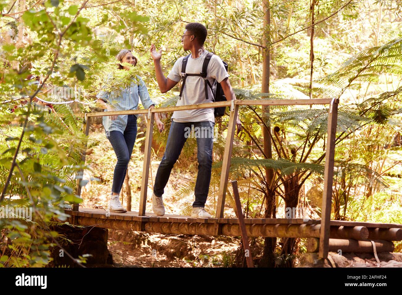 Two young adult friends hiking in a forest crossing a footbridge, full length Stock Photo