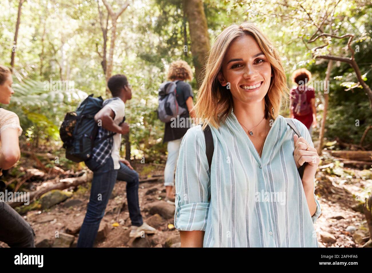 Waist up portrait of smiling millennial white woman hiking in a forest with her friends, close up Stock Photo