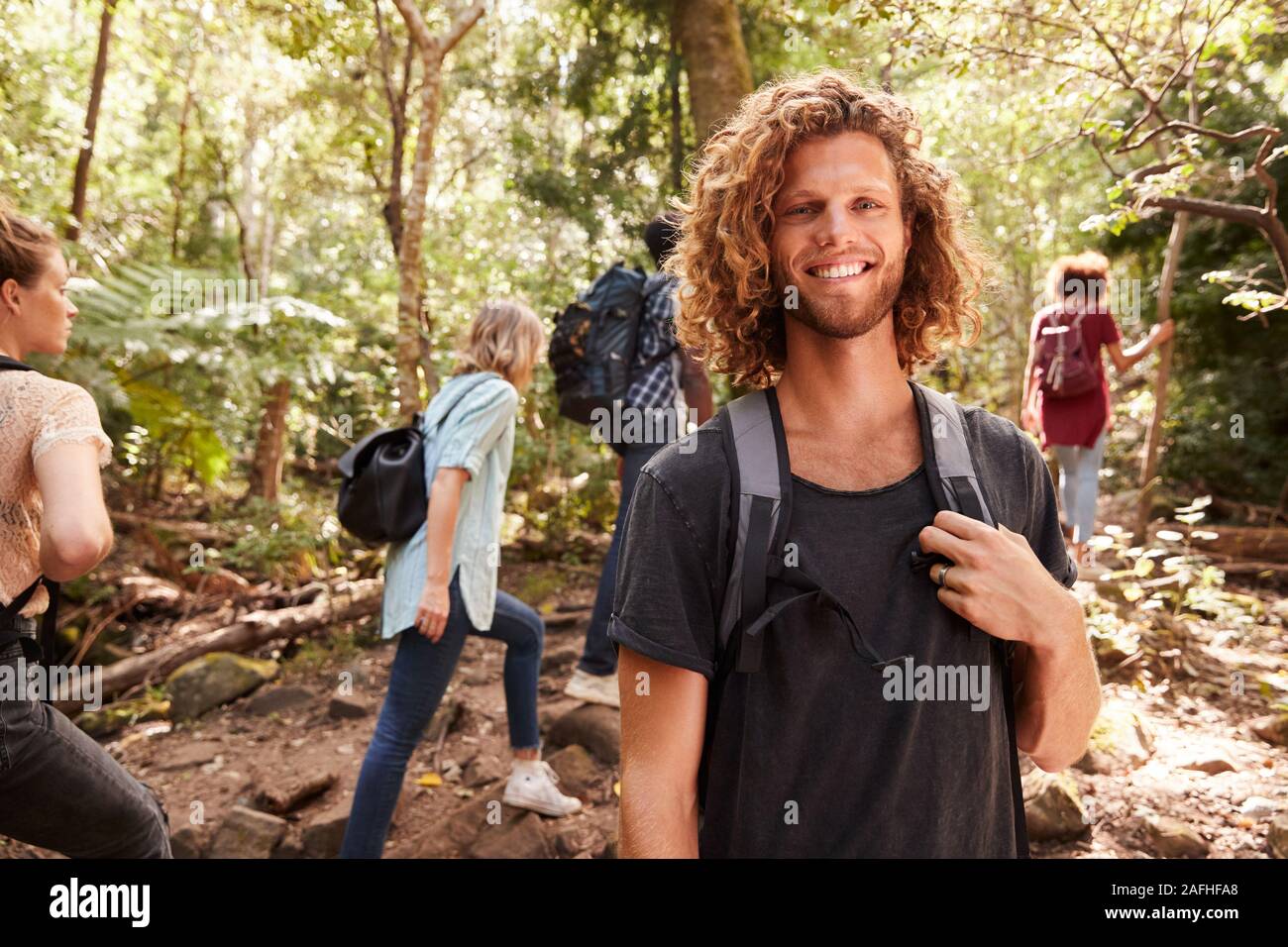 Waist up portrait of smiling millennial white man hiking in a forest with friends, close up Stock Photo