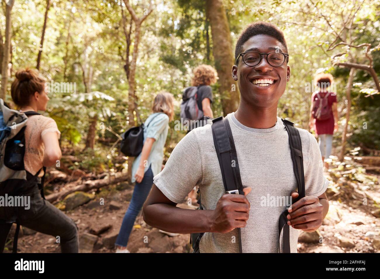 Waist up portrait of smiling millennial African American man hiking in a forest with friends, close up Stock Photo