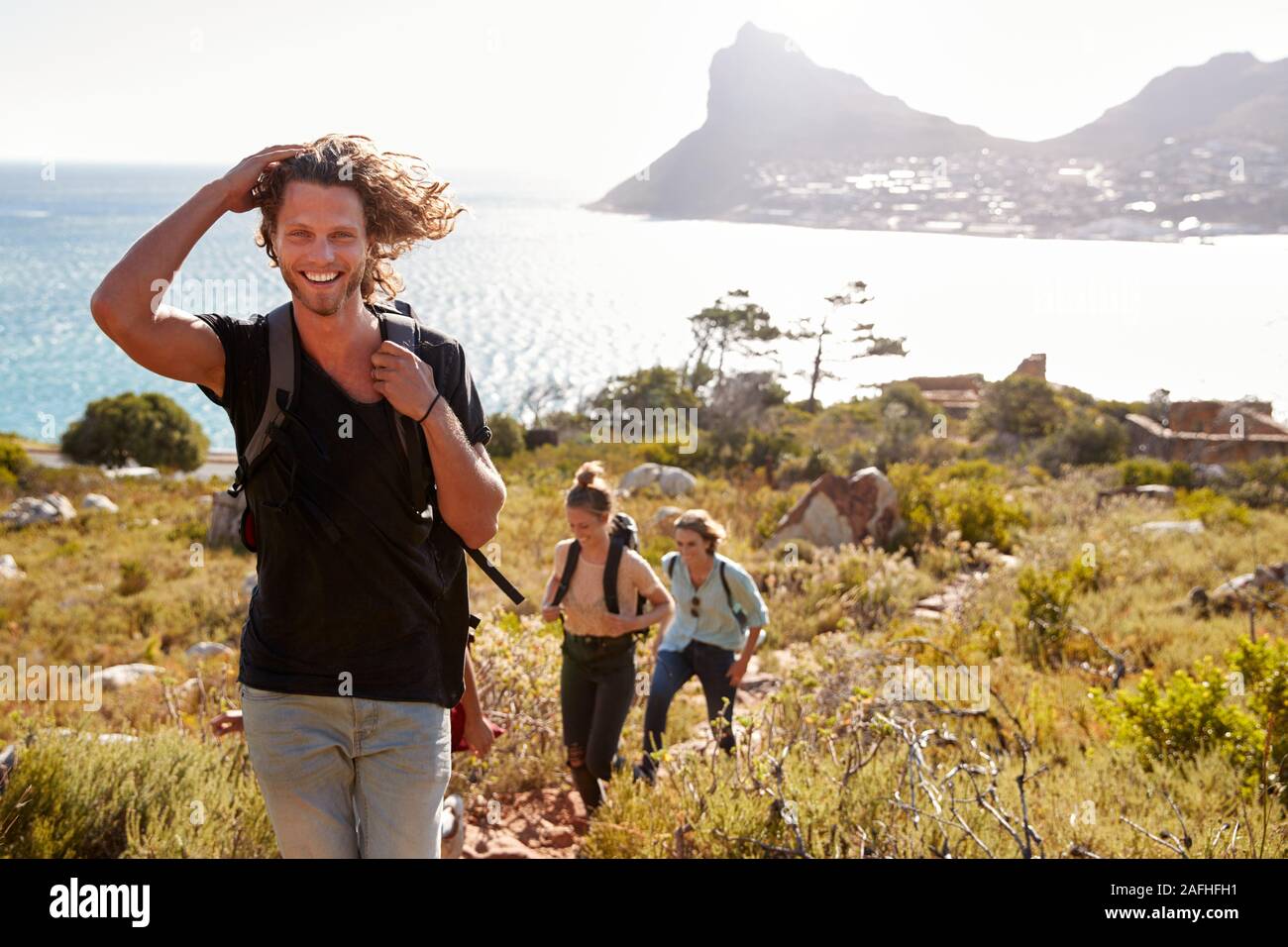 Young adult white man hiking with friends in countryside by the coast smiling to camera Stock Photo