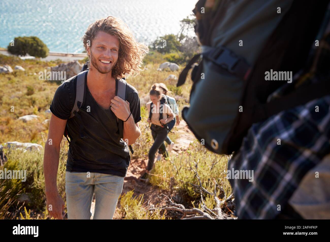 Young adult white man hiking with friends in countryside by the coast, smiling to camera Stock Photo