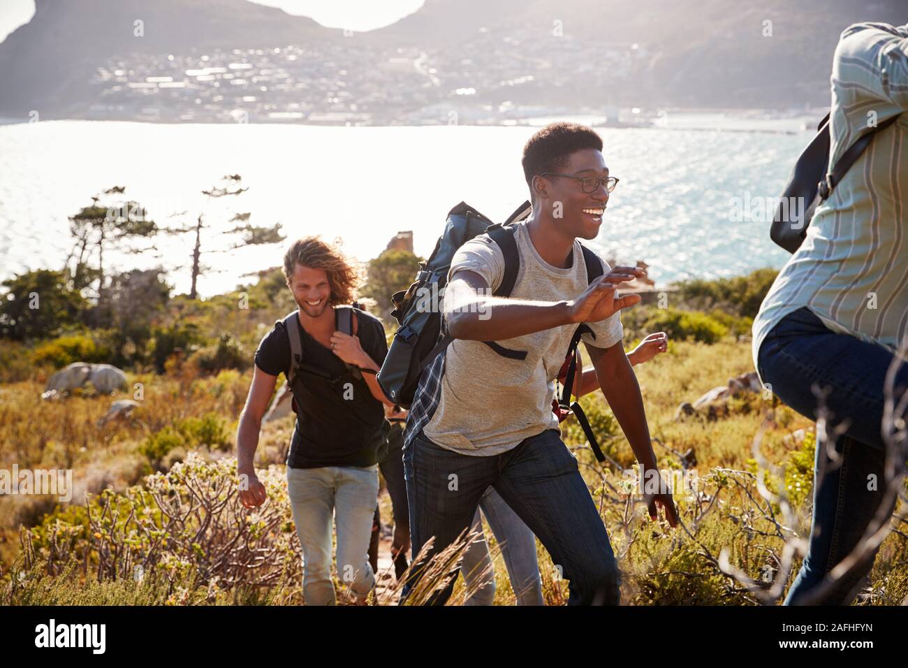 Happy young adult friends hiking uphill near the coast, close up, backlit Stock Photo