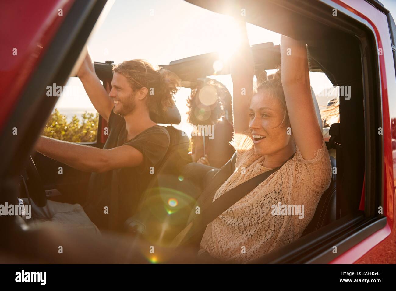 Excited millennial friends on a road trip vacation driving in an open car, close up, lens flare Stock Photo