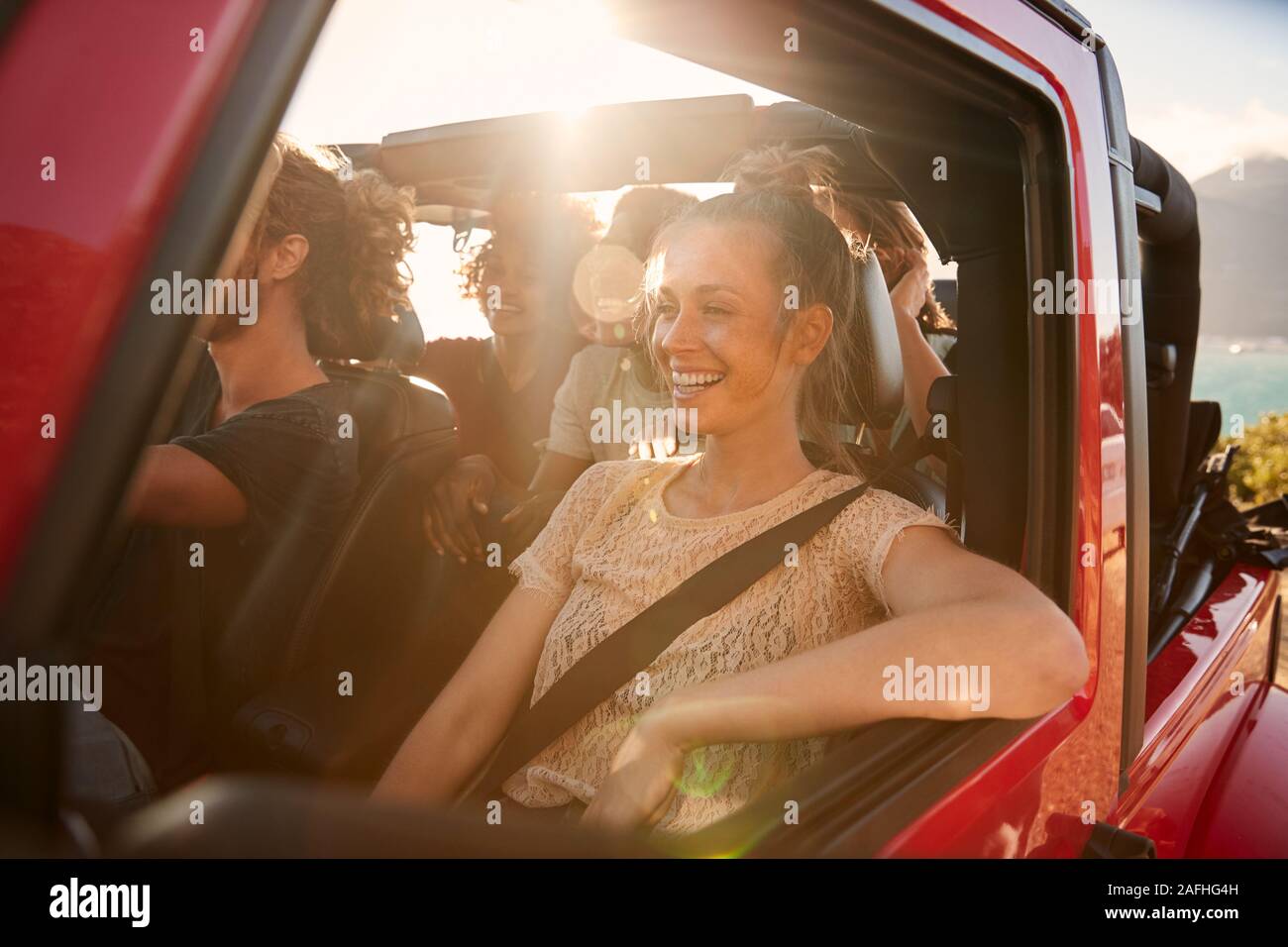 Happy millennial friends on a road trip vacation driving in an open car, close up, lens flare Stock Photo