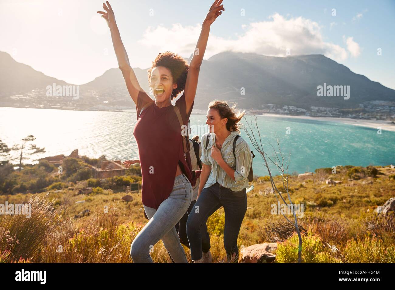 Millennial African American woman hiking by the coast with a friend celebrates reaching summit Stock Photo