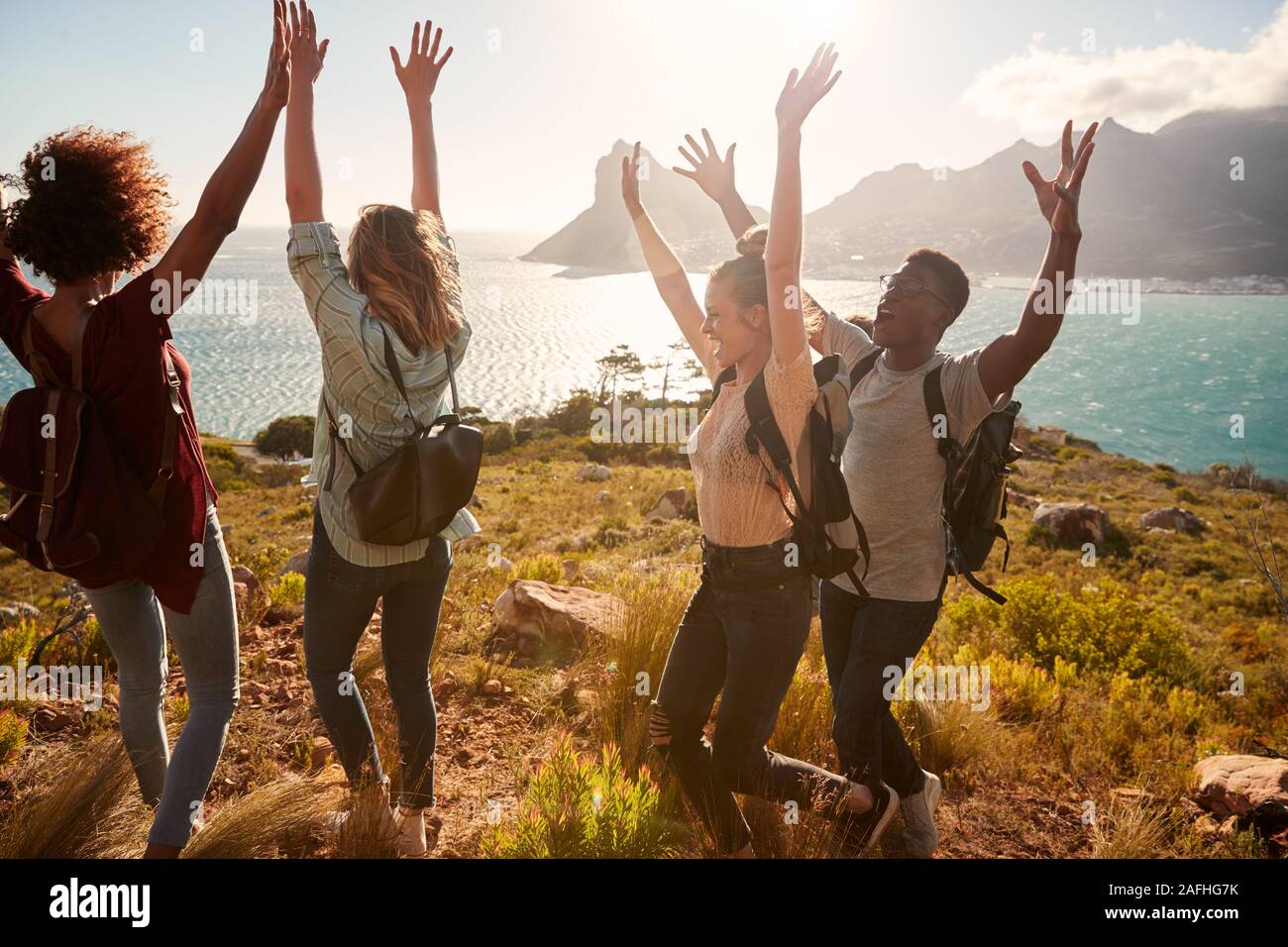 Millennial friends on a hiking trip celebrate reaching the summit, cheering with arms in the air Stock Photo