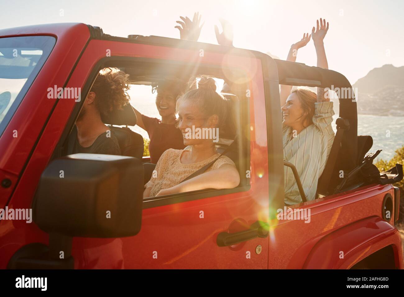 Excited young adult friends on a road trip vacation driving in an open top car, lens flare Stock Photo