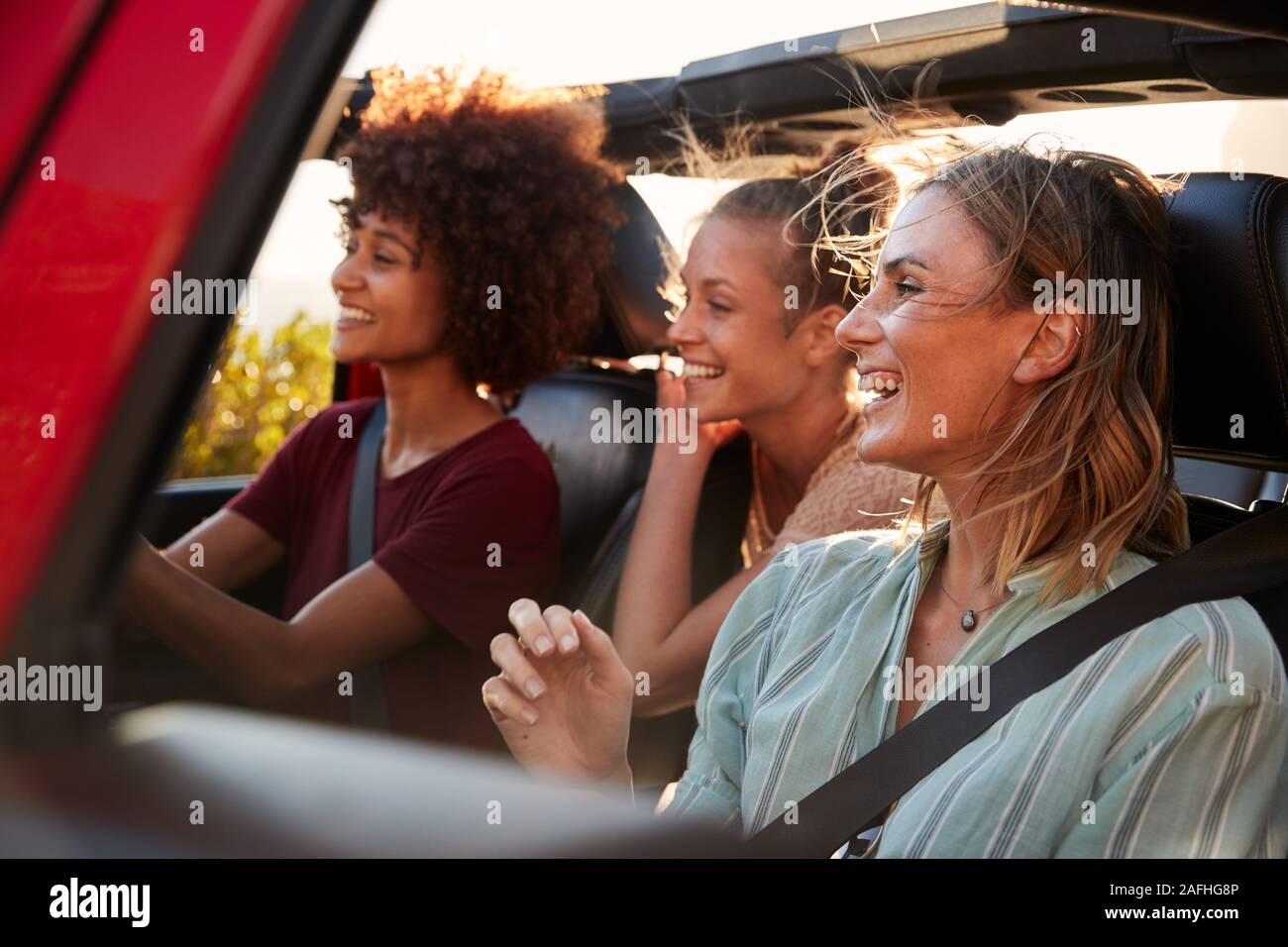 Three millennial female friends on a road trip driving together in an open jeep, close up Stock Photo