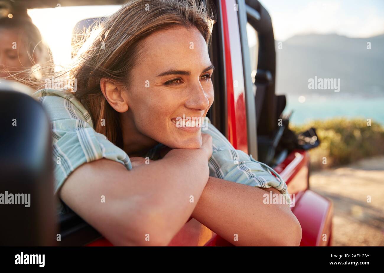 Millennial white woman on a road trip with friends leaning on car door enjoying view, close up Stock Photo
