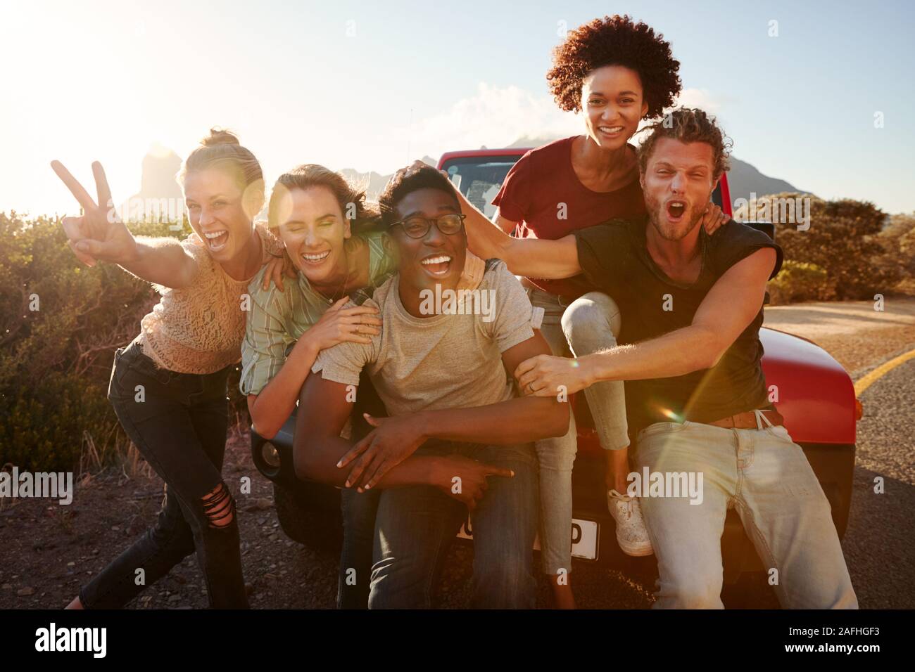 Five millennial friends on a road trip have fun posing for photos at the roadside, lens flare Stock Photo