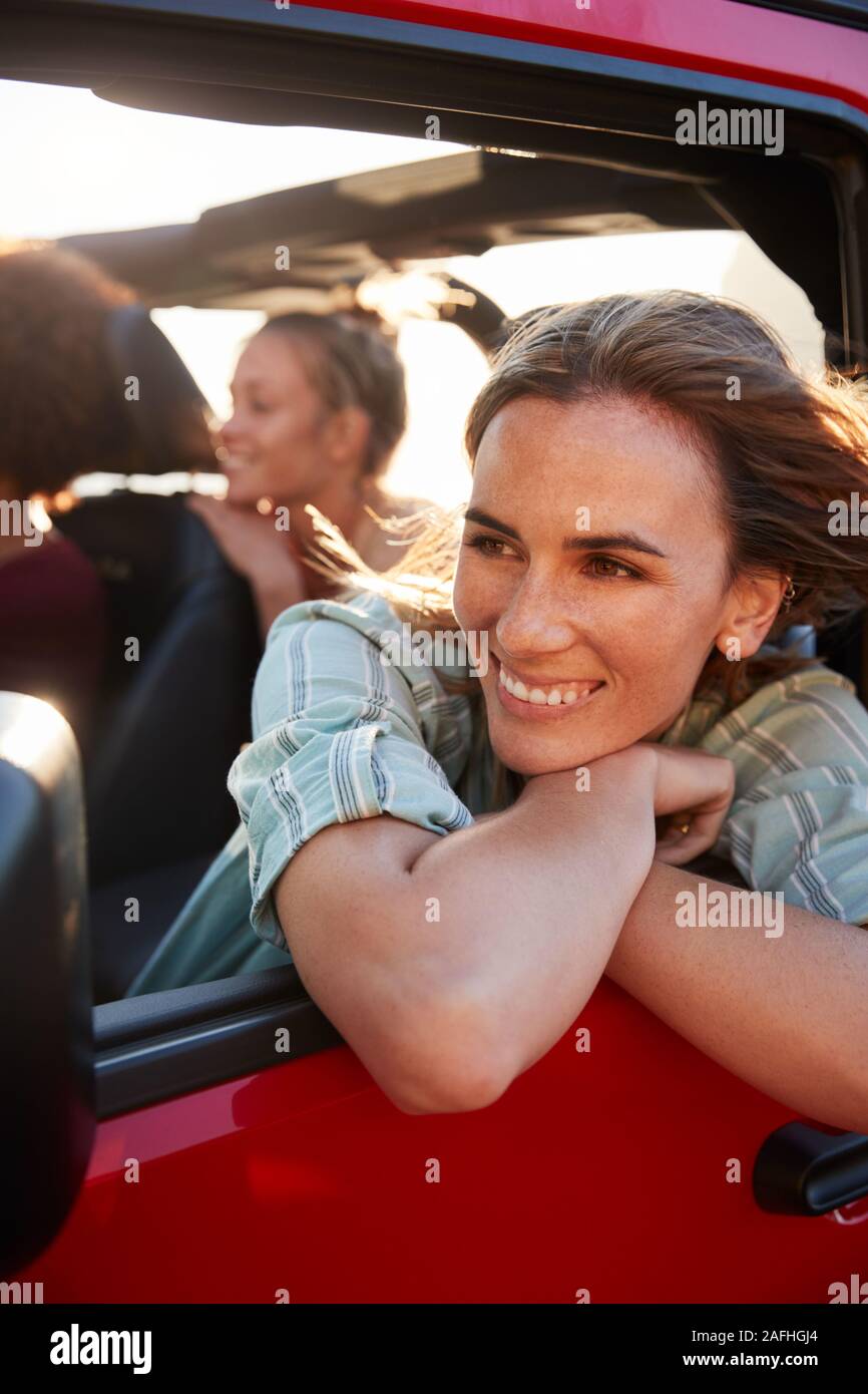 Millennial white woman on a road trip with friends, leaning looking out of car window, vertical Stock Photo