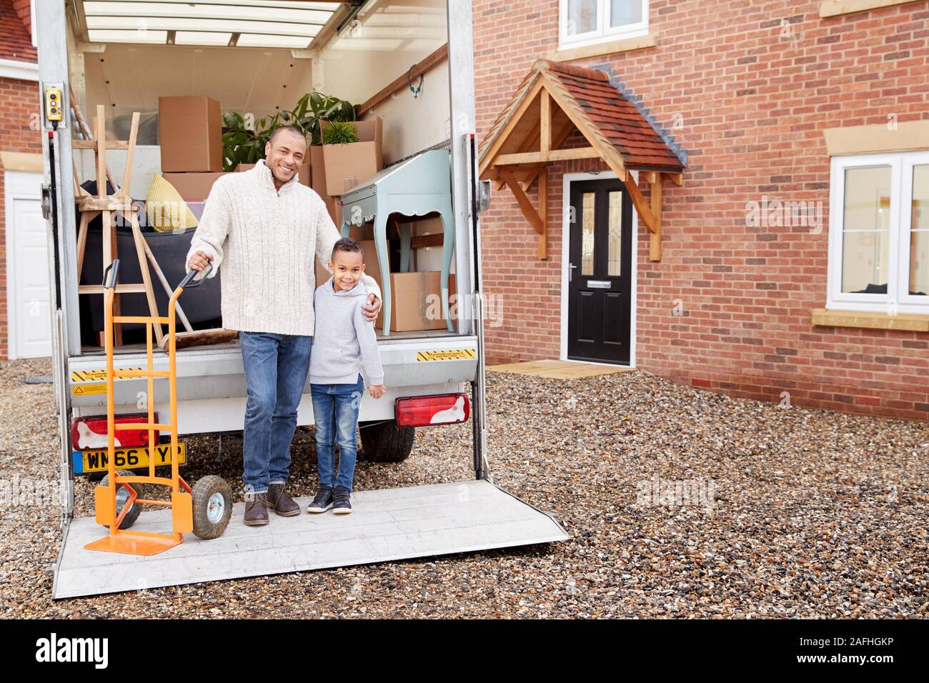 Portrait Of Father And Son Unloading Furniture From Removal Truck Into New Home Stock Photo