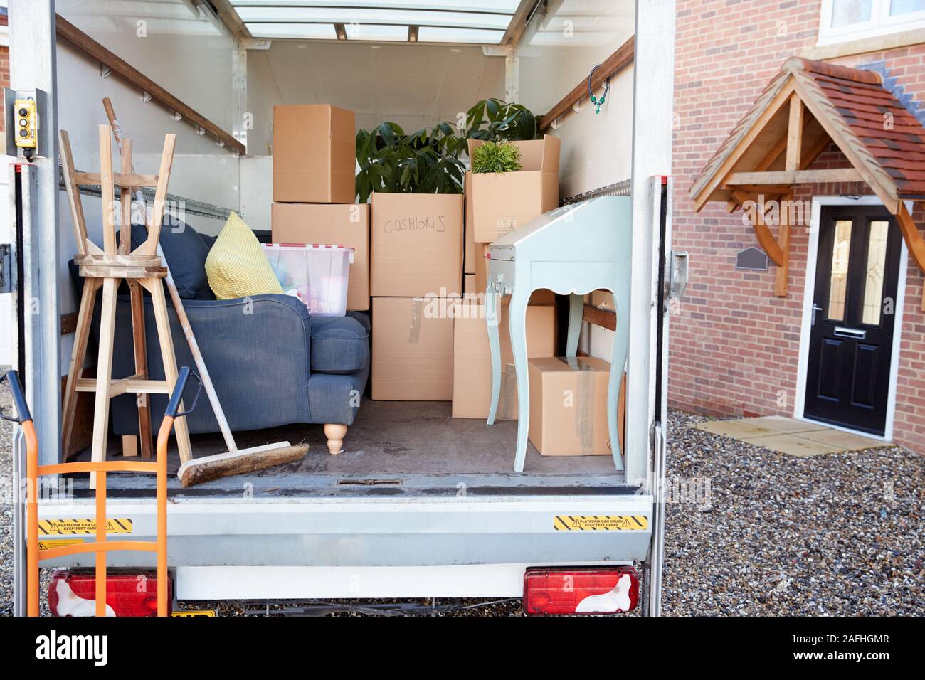 Removal Truck Waiting To Be Unloaded Outside New Home On Moving Day Stock Photo