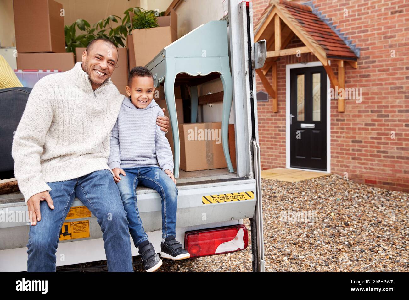 Portrait Of Father And Son Unloading Furniture From Removal Truck Into New Home Stock Photo