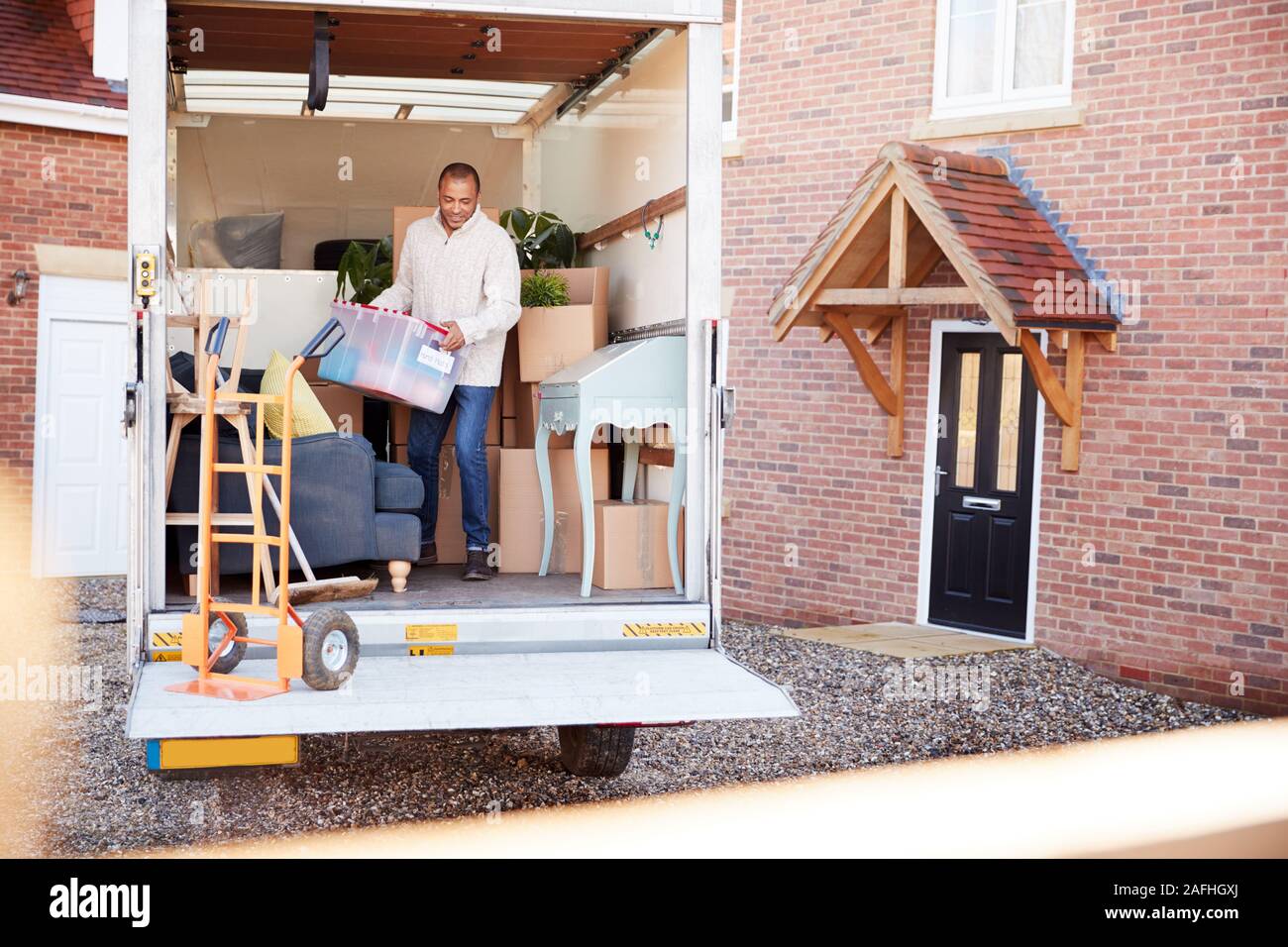 Man Unloading Furniture From Removal Truck Outside New Home On Moving