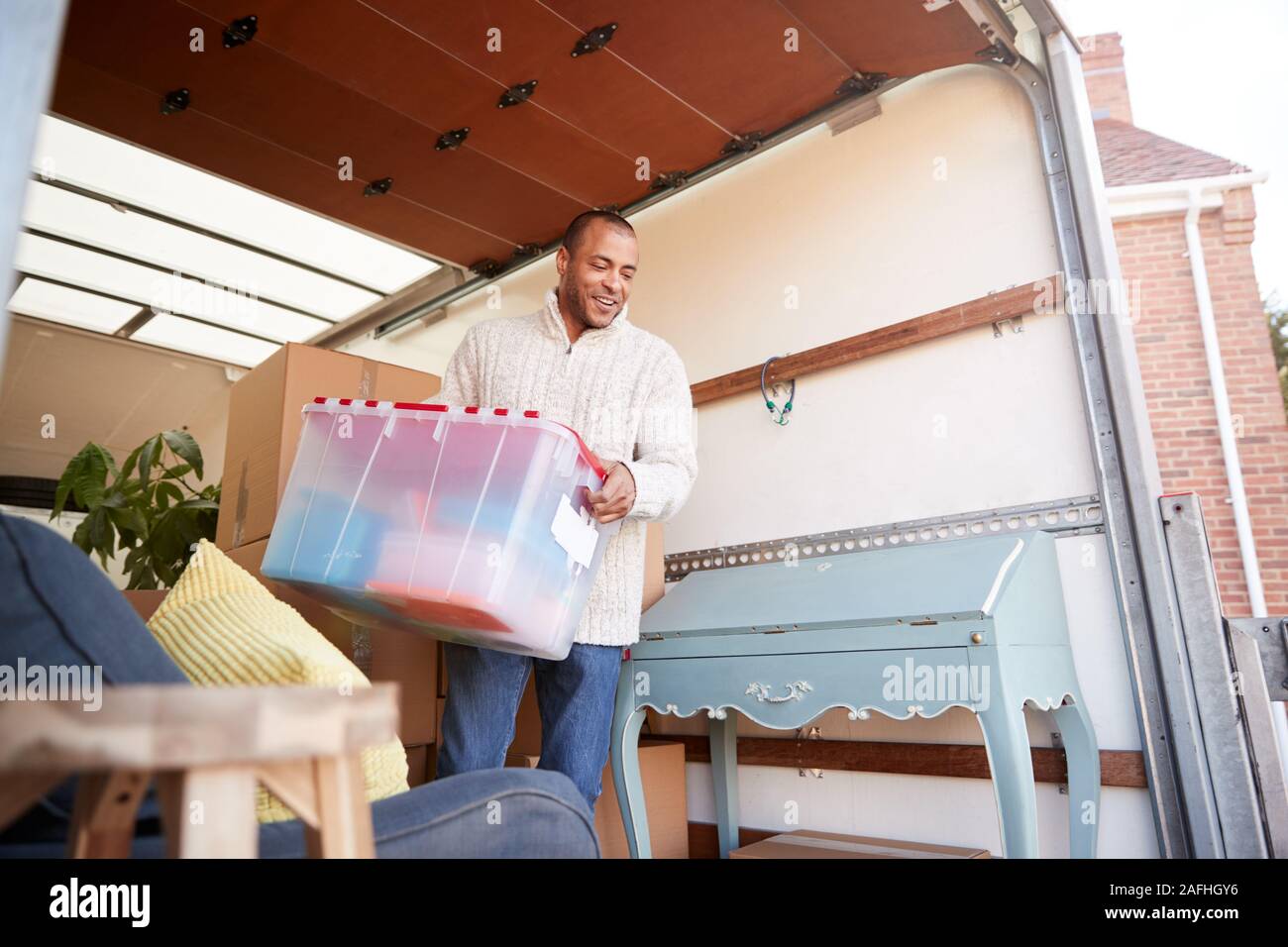 Man Unloading Furniture From Removal Truck Outside New Home On Moving