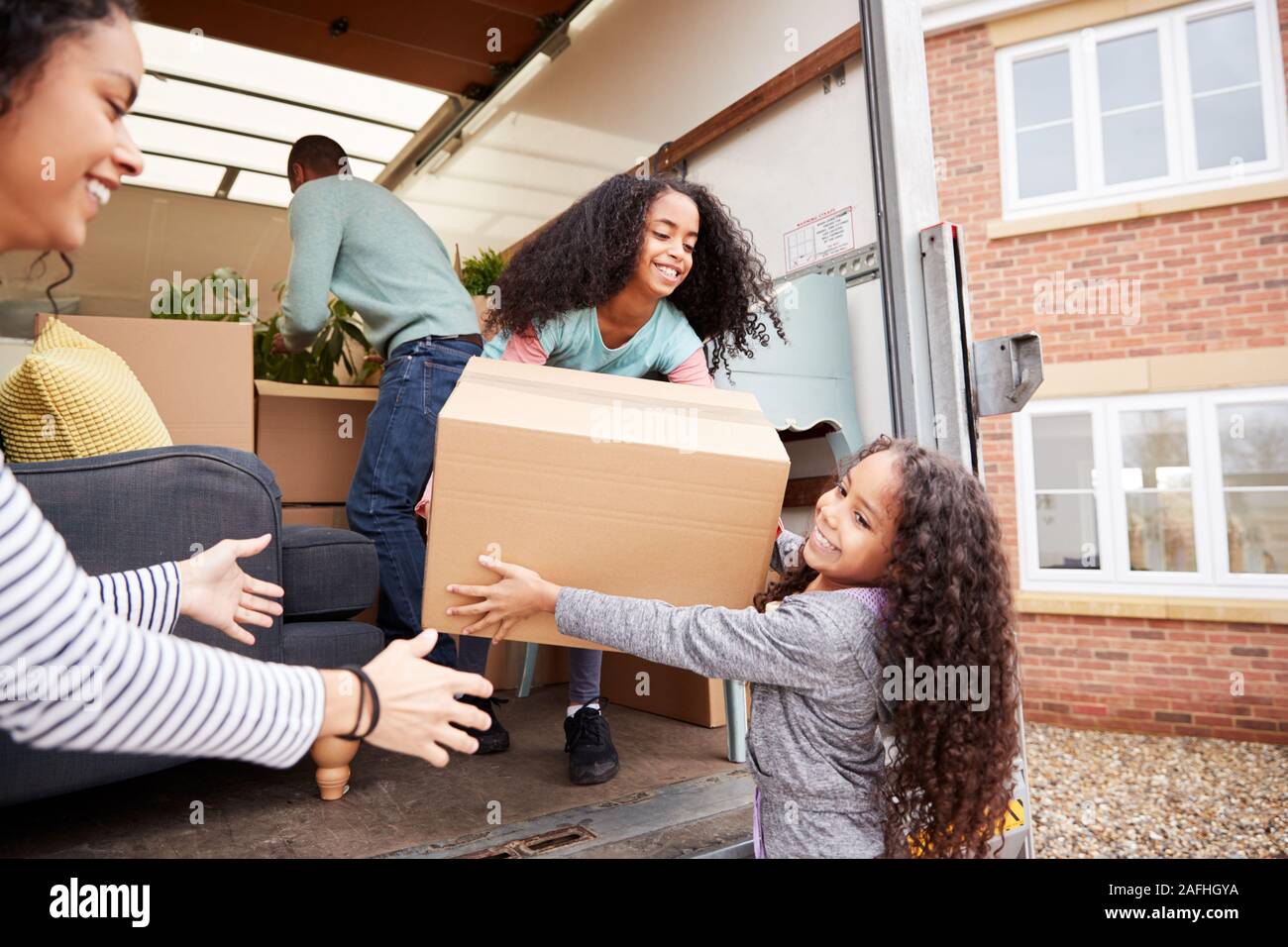 Family Unloading Furniture From Removal Truck Into New Home Stock Photo
